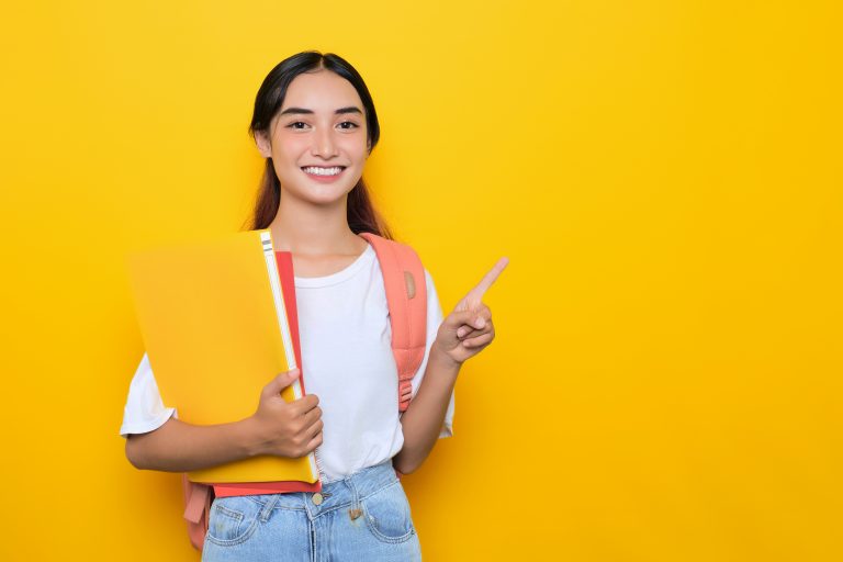 cheerful pretty young student girl wearing backpack pointing blank space isolated yellow background scaled